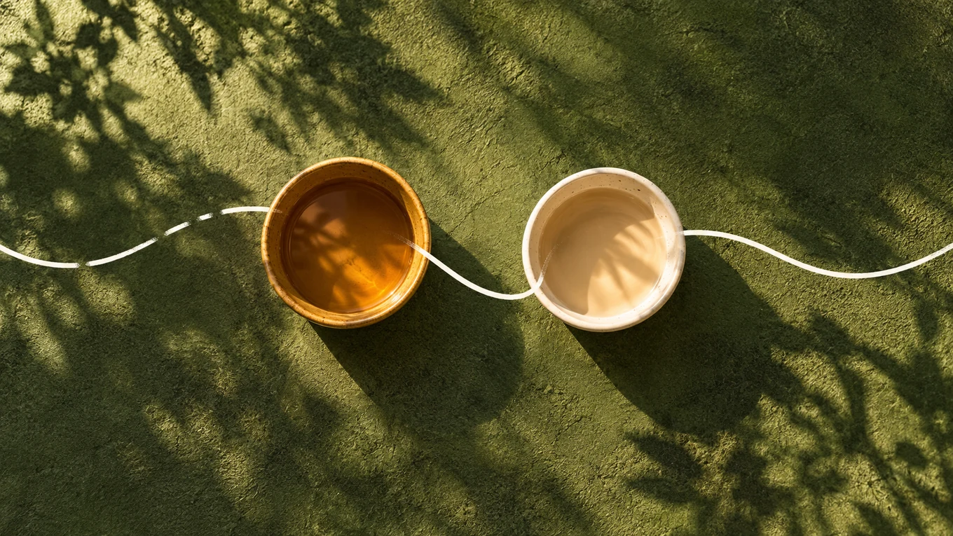 Two cups joined by a flowing white line on an olive-green surface